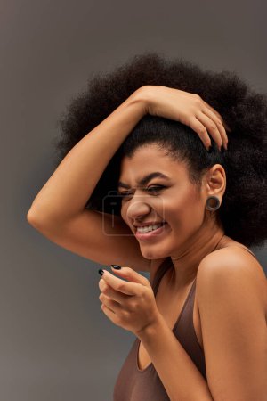 modelo femenino afroamericano alegre en ropa interior pastel sonriendo felizmente, concepto de moda