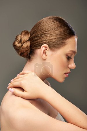 Téléchargez les photos : Vue latérale de jeune femme avec un chignon à cheveux et une peau parfaite posant sur fond gris, charmant - en image libre de droit