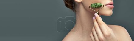 Téléchargez les photos : Jeune femme avec peau parfaite massage visage avec rouleau de jade sur fond gris, bannière de soins de la peau - en image libre de droit