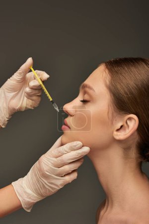 Photo for Esthetician in medical glove holding syringe near lips of young woman on grey background, filler - Royalty Free Image