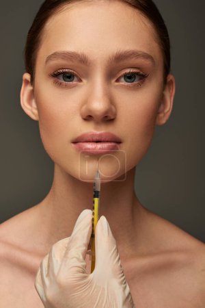 Photo for Esthetician in medical glove holding syringe near young woman on grey background, lip filler - Royalty Free Image