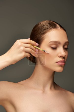 pretty young woman holding syringe near face on grey background, skin rejuvenation concept