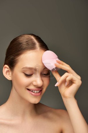 happy woman holding cleansing brush on grey background, beauty gadget and skin care concept