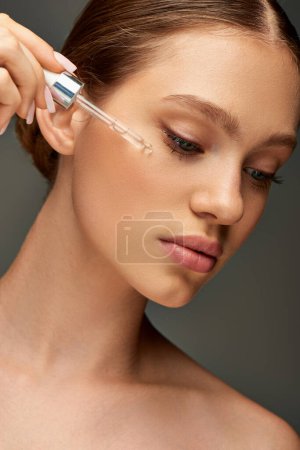 Photo for Young woman with glowy skin holding dropper with serum near face on grey background, hydration - Royalty Free Image