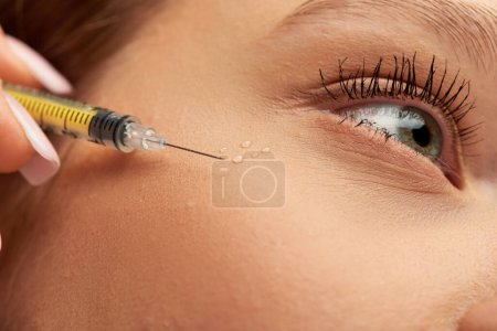 close up of syringe with hyaluronic acid or filler near face of young woman on grey background