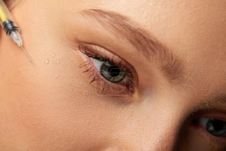 close up of syringe with hyaluronic acid or filler near face of woman on grey background, beauty