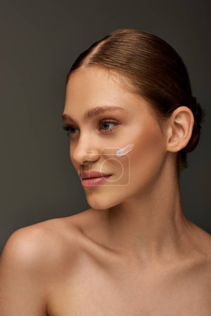 beautiful young woman with cream on face and bare shoulders posing on grey background, look away