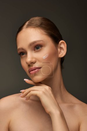 pretty young woman with cream on face and bare shoulders posing on grey background, look away