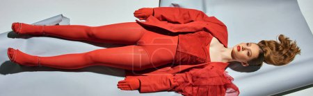 Photo for Top view of young model in red outfit  lying on grey background, woman acting like a doll banner - Royalty Free Image