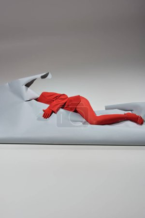 femme recadrée en tenue rouge avec des gants et des collants couchés près du papier déchiré sur fond gris
