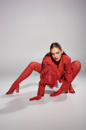 young model in stylish red attire with high heels and bright tights posing on grey background