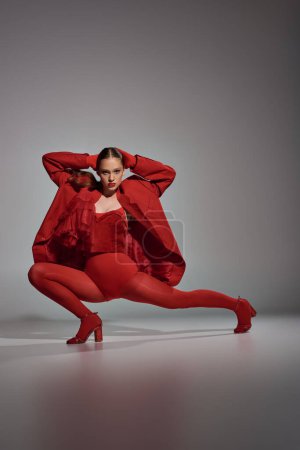 confident model in stylish red outfit with tights and high heels posing on grey background