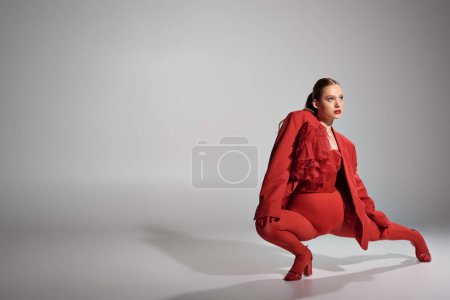 high fashion model in stylish red outfit with tights and high heels posing on grey background