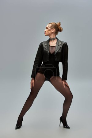 trendy model with pearl pins in hair posing in leather jacket and high heels on grey background