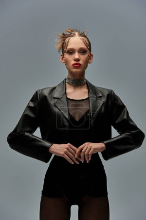 stylish woman with pearls in hair posing in leather jacket and black tights on grey background