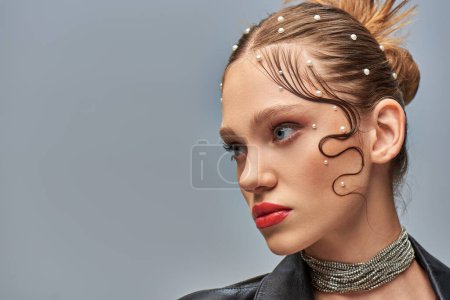 retrato de modelo joven glamuroso con alfileres de perlas en el pelo y labios rojos posando sobre fondo gris