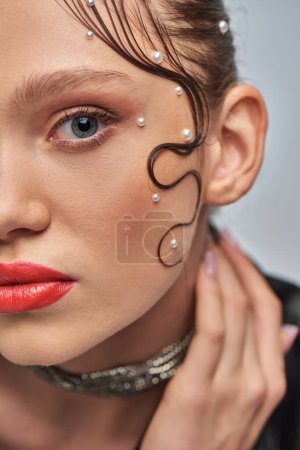 Foto de Primer plano de mujer joven glamurosa con alfileres de perlas en el pelo y labios rojos posando sobre fondo gris - Imagen libre de derechos