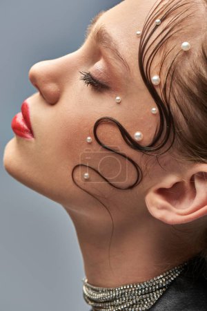 Nahaufnahme eines hübschen jungen Models mit trendigen Perlstiften im Haar und roten Lippen vor grauem Hintergrund