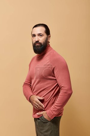 Porträt, fokussierter und gutaussehender Mann mit Bart posiert in rosa Rollkragenpullover auf beigem Hintergrund