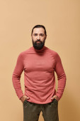 portrait, handsome focused man with beard posing in pink turtleneck jumper  on beige background mug #684012966