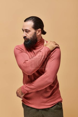 portrait, powerful handsome man with beard posing in pink turtleneck jumper on beige background mug #684013134