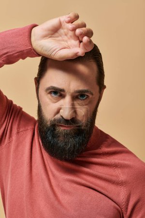 portrait of handsome man with beard posing in pink turtleneck jumper on beige background, serious