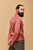 handsome and serious man with beard posing in pink turtleneck jumper on beige background, portrait t-shirt #684013462