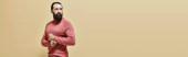 serious good looking man with beard posing in pink turtleneck jumper on beige backdrop, banner magic mug #684013544
