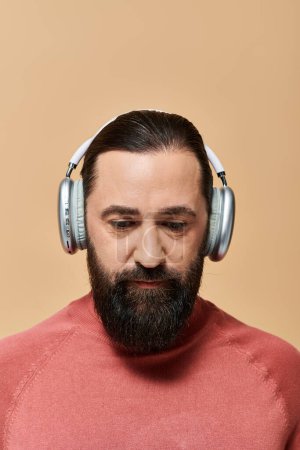 handsome bearded man in pink turtleneck jumper listening music in wireless headphones on beige