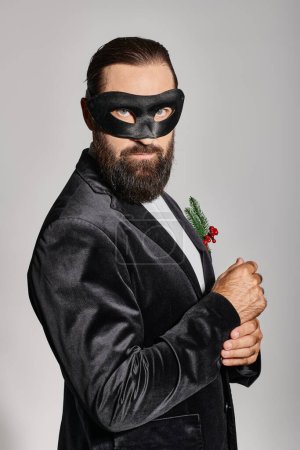 Baile de máscaras de Navidad, hombre barbudo guapo en máscara de carnaval y traje elegante sobre fondo gris
