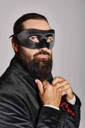 Mascarada de Navidad, hombre barbudo guapo en máscara de carnaval y traje elegante sobre fondo gris