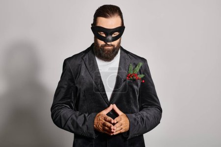 Masquerade ball, concentrated bearded man in carnival mask and elegant formal wear on grey backdrop
