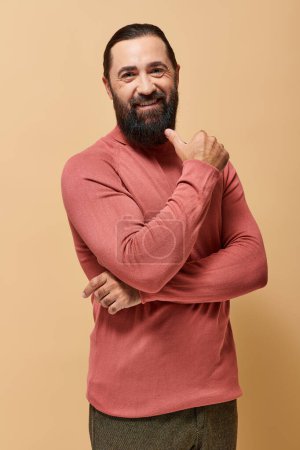 cheerful bearded man in casual turtleneck jumper looking at camera on beige backdrop, male fashion