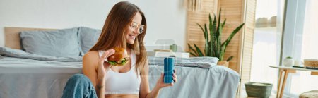 cheerful woman with glasses holding delicious burger and soft drink and smiling happily, banner