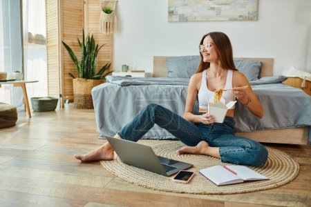 Photo for Cheerful attractive woman in comfy homewear sitting on floor with noodles while working remotely - Royalty Free Image