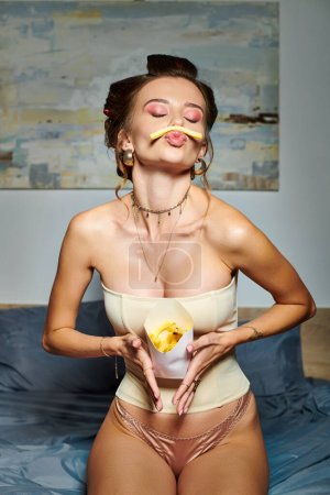 alluring beautiful woman with hair curlers and accessories in corset posing in motion with fries
