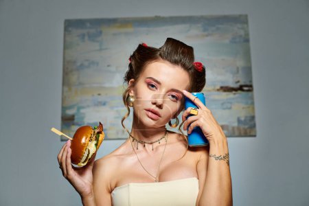 appealing sexy woman in beige corset with hair curlers posing with burger and soda looking at camera
