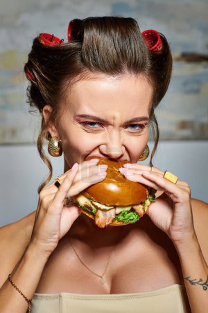 Téléchargez les photos : Belle femme sexy en corset beige avec accessoires manger énorme hamburger et regarder la caméra - en image libre de droit