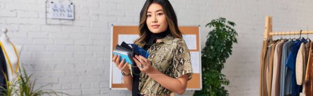 joven estilista asiático de moda con muestras de color mirando a la cámara en atelier privado, bandera
