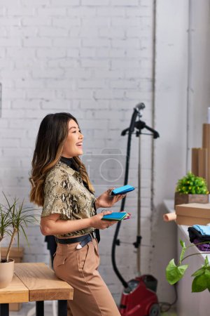 Photo for Side view of joyful designer holding color swatches in clothes atelier, private fashion business - Royalty Free Image