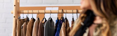 Téléchargez les photos : Vue recadrée du créateur de mode flou près du rack avec des vêtements sur mesure à la mode dans l'atelier, bannière - en image libre de droit