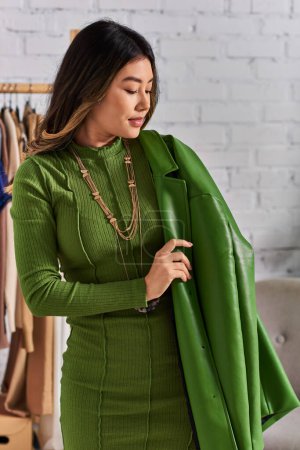 Téléchargez les photos : Couturière asiatique tendance posant en veste en cuir vert dans un atelier de mode privé, petite entreprise - en image libre de droit