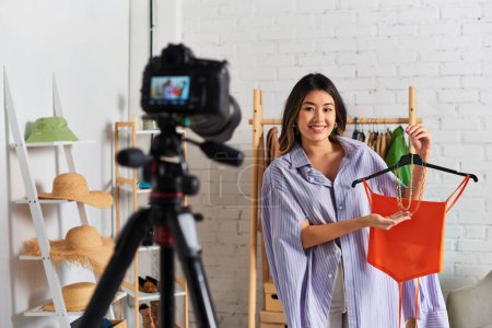 Téléchargez les photos : Styliste asiatique créatif montrant crop top et accessoires pendant vlog mode dans un atelier privé - en image libre de droit