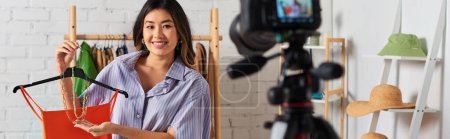 Téléchargez les photos : Heureux asiatique designer montrant crop top et accessoires pendant vlog mode dans atelier privé, bannière - en image libre de droit