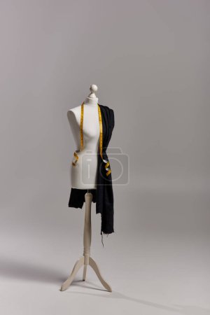 mannequin sur trépied avec tissu et ruban à mesurer sur fond gris, concept d'entreprise de mode