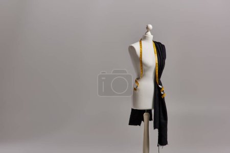 mannequin on tripod with quality fabric and measuring tape on grey background, dressmaking business