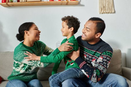 Foto de Familia afroamericana feliz sentado en el sofá y sonriendo alegremente el uno al otro, Navidad - Imagen libre de derechos