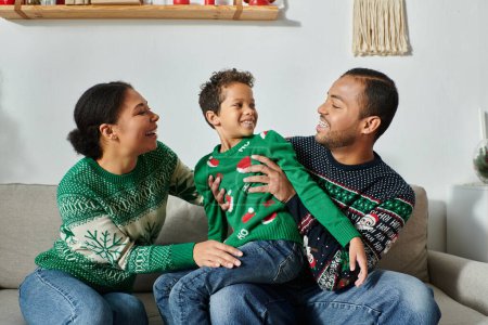 alegre afroamericano padres con su hijo sentado en regazo vistiendo caliente Navidad suéteres