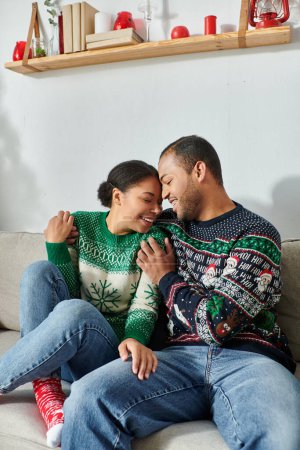 Afrikanisch-amerikanisches Liebespaar in Winterpullovern, die sich mit geschlossenen Augen auf dem Sofa warm umarmen, Weihnachten