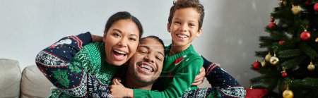 fröhliche afrikanisch-amerikanische Familie in Pullovern, die sich warm umarmen und in die Kamera lächeln, Weihnachten, Banner